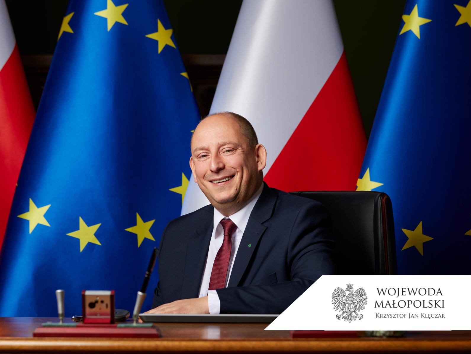 Krzysztof Jan Klęczar, Wojewoda Małopolski siedzący przy biurku na tle flag Polski