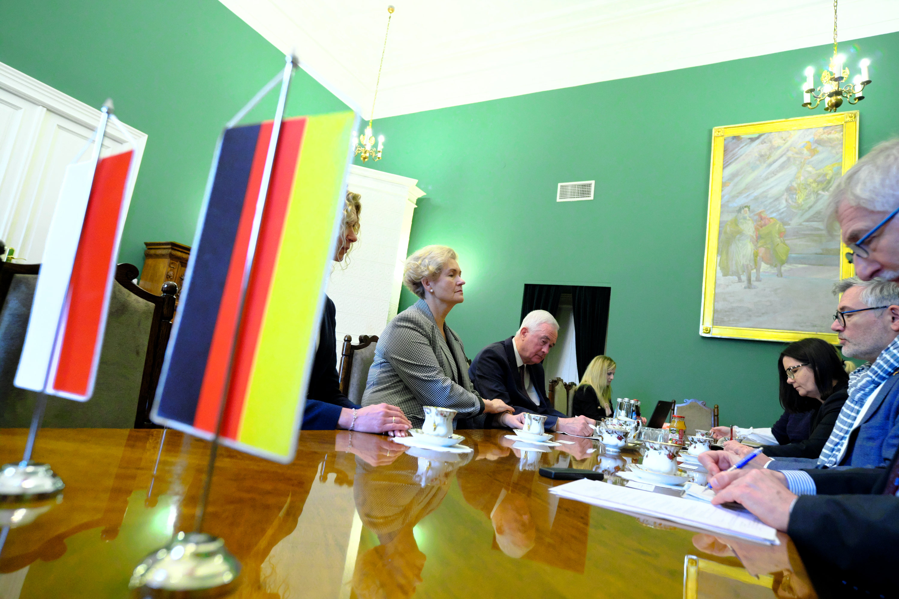 Na zdjęciu wnętrze gabinetu I wicewojewody małopolskiej Elżbiety Achinger podczas spotkania z delegacją niemiecką. Na pierwszym planie widoczne flagi: polska, niemiecka. W tle grupa ludzi przy stole. 